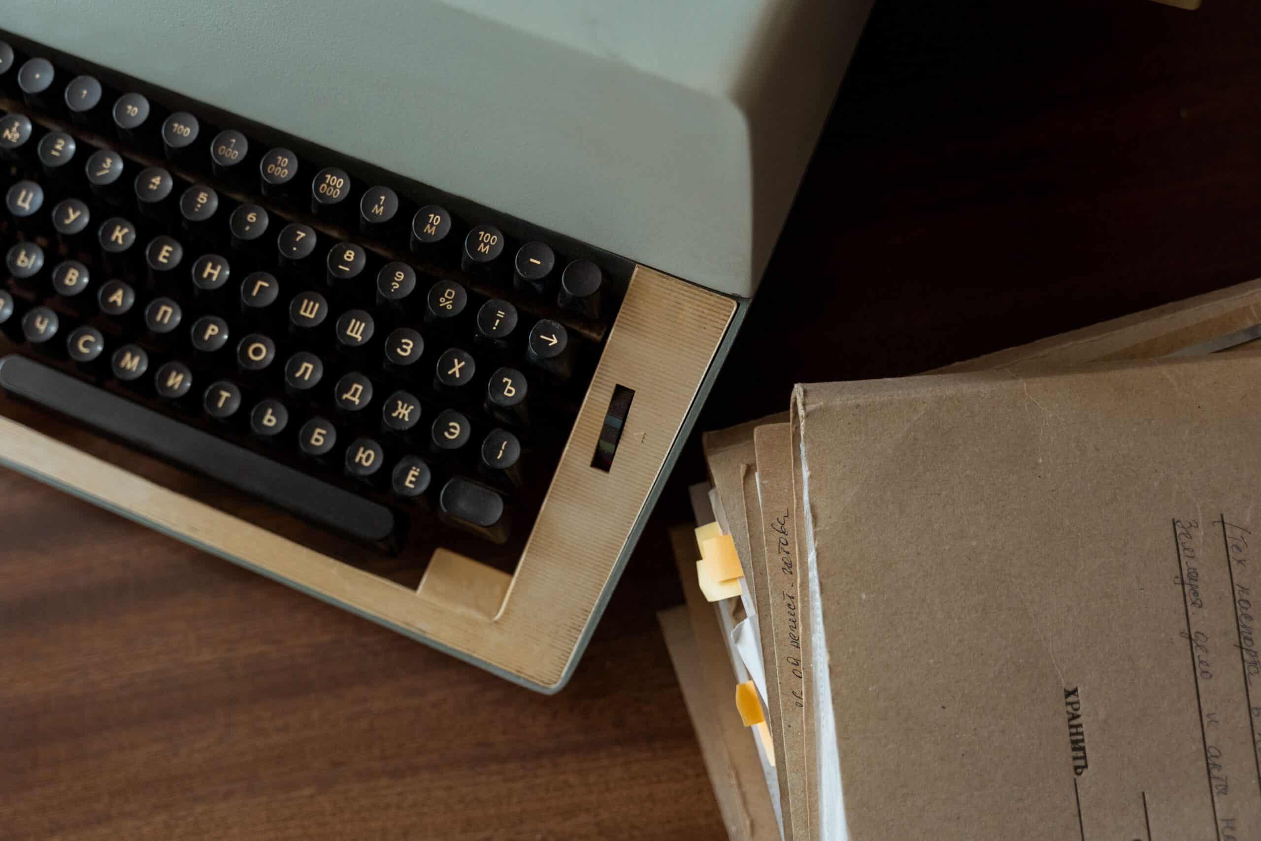 A classic vintage typewriter alongside stacked brown paper documents on a wooden desk.